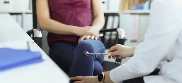Close-up of doctor neurologist checking knee reflexes of female patient with percussion hammer in clinic. Neurology, checkup, medicine, diagnostics concept