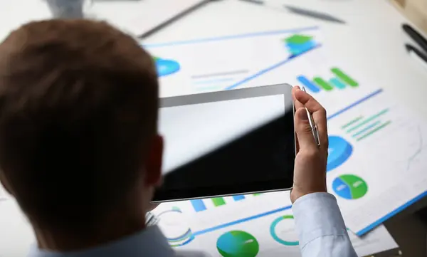 Close-up of man use tablet, black screen, papers with diagrams and charts on desktop. Business, strategy, statistics, report, mockup concept. Copy space