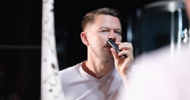 Красивый Молодой Человек Снимает Волосы Носа Триммером Перед Зеркалом Концепция — стоковое видео