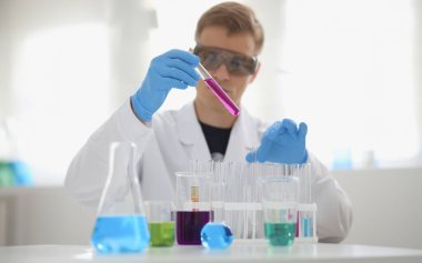 Erkek bir kimyager elinde cam test tüpü tutarak potasyum permanganatın sıvı çözeltisini taşır. Kimyasal imalatı kullanarak çeşitli reaksiyonlar uygular.