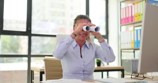 遊び心のある実業家がテーブルに座り 双眼鏡を通して紙巻きを見ています オフィスの同僚を観察し ビジネスアイデアを探す — ストック動画
