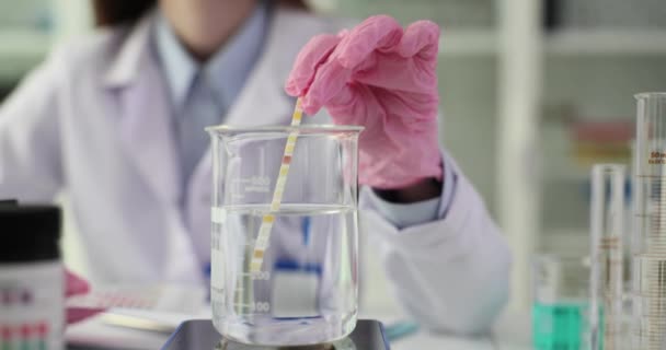 科学者は実験室で天然飲料水のサンプルを試験管に中性リトマス紙を保持しています 水の純度をチェックする — ストック動画