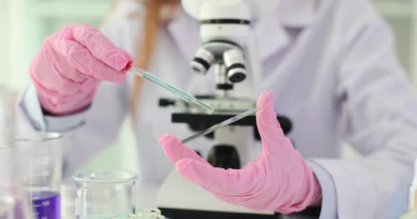 科学家在实验室把蓝色液体的样品放到显微镜滑块上 生物学家实验室助理化学家滴在玻璃滑道和显微镜上检查液体滴 — 图库视频影像
