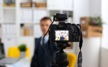 Erkek takım elbise ve kravat göstermek onaylamak işareti kol yapma promo videoblog veya fotoğraf oturumunda office video kamera tripod taşımak için. Vlogger tanıtım selfie çözüm ya da Finans Danışmanı yönetimi bilgileri