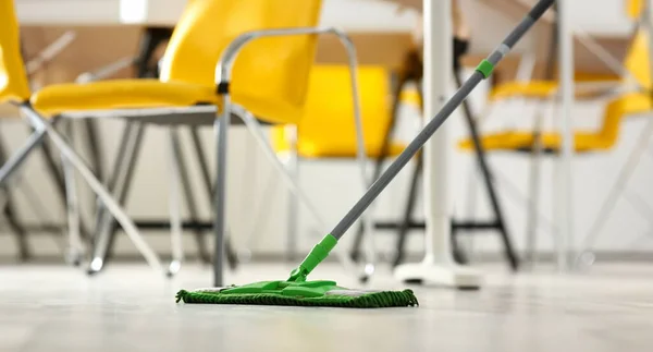 Green plastic mop cleaning laminated light dirty floor closeup