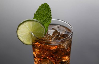 Derisi yüzülmüş mutfak arka planında iç mekan ürünleri için cam parmak izinde viski bulunan kokteyl kola. Moda mobilyalar, siyah gri eğimli dilimlenmiş meyve ve buz baskı..