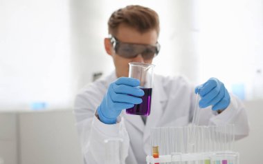 Erkek bir kimyager elinde cam test tüpü tutarak potasyum permanganatın sıvı çözeltisini taşır. Kimyasal imalatı kullanarak çeşitli reaksiyonlar uygular.