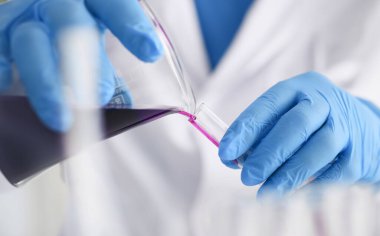 Erkek bir kimyager elinde cam test tüpü tutarak potasyum permanganatın sıvı çözeltisini taşır. Kimyasal imalatı kullanarak çeşitli reaksiyonlar uygular.