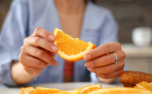 A woman holds a slice of sliced orange in her hand during an early breakfast in the kitchen the concept of a healthy diet