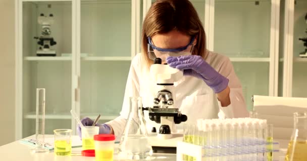 科学者の医師は顕微鏡を観察し 報告書にメモを書いている 研究室での尿検査 — ストック動画