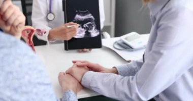Kadın doğum uzmanı test sonuçlarını tablet bilgisayarla ilgili kocaya ve klinikteki hamile kadına açıklıyor. Bebek bekleyen çift doktorlarını dikkatle dinliyor.