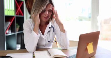 Kadın, masada oturan bir doktor başını tutar, yakın plan. Tıbbi personel yükle, işte stres yap.