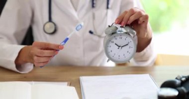 Elinde çalar saati ve diş fırçası olan bir doktor. Yakın plan. Ağız boşluğu için hijyenik prosedür, diş fırçalama.