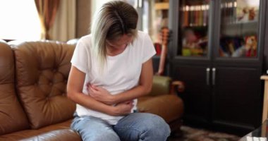 Kanepede oturan bir kadın karnına masaj yapıyor, yakın plan, yavaş çekim. Karın ağrısı konsepti, hastalık