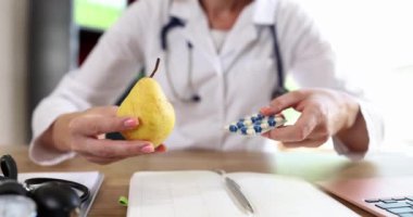 Kadın bir doktor. Hapları ve armudu tutuyor. Yakın plan. Beslenme uzmanını ziyaret etmek, diyet randevusu
