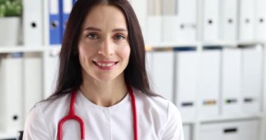 4K numaralı klinikte ağır çekimde beyaz üniformalı gülümseyen kadın doktor portresi. Sağlık hizmeti kavramı