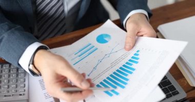 Takım elbiseli bir işadamı, elinde grafiklerle belgeleri inceliyor. 4K yavaş çekim. İş analizi kavramı