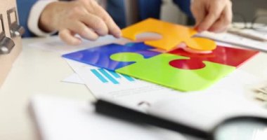 İş adamı renkli yapbozun son parçasını masa başına koyuyor. 4K film yavaş çekim. Takım çalışması konsepti