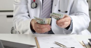 Erkek doktor masada oturuyor ve $4K 'lık banknotları sayıyor. Tıp konseptinde yolsuzluk