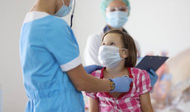 Doktor, klinikteki resepsiyonda steteskopla nefes alan kızı dinliyor. Çocuk konseptinde zatürree ve koronavirüsün belirtileri