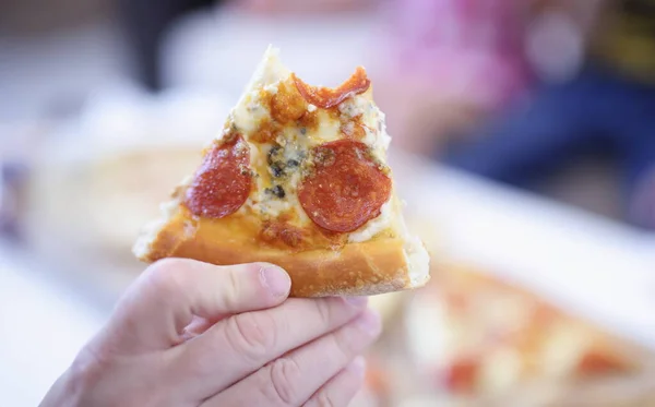 Slice of pizza with sausage in hand on pizza background. Snacks with proper nutrition concept