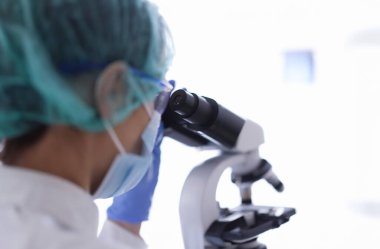 Gözlüklü ve tıbbi maskeli doktor laboratuvar asistanı mikroskoptan bakıyor. Laboratuvar araştırma konsepti