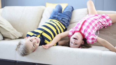 Oğlan ve kız kanepede baş aşağı uzanıp gülüyorlar. Mutlu çocukluk kavramı