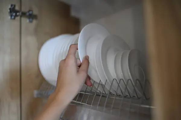 Womans hand pulls clean white dishes out of kitchen cabinet. Household helpers services concept
