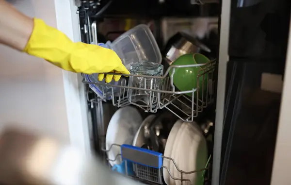 Clean dishes are taken out of the open dishwasher in yellow glove. Household appliances for kitchen concept