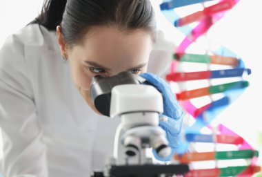 Laboratuvarda DNA molekül modelinin yanında mikroskoptan bakan kadın bilim adamı. Bilimsel genetik araştırma kavramı