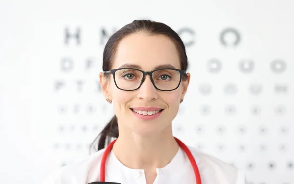 Woman ophthalmologist with glasses standing against background of table for eye test. Laser vision correction concept