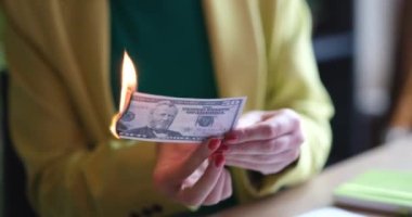 Businesswoman burns fifty dollar banknote at workplace. Economic crisis or inflation concept