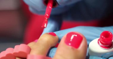 Manicurist applies red polish to client toenails. Beautiful red pedicure in beauty salon concept