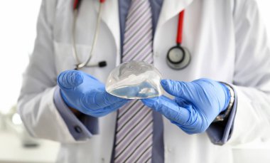 Mavi koruyucu eldivenli erkek doktor elinde yeni moda silikon göğüs implantı var. Plastik düzeltme cerrahi konsepti