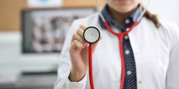 Close-up view of faceless medical female worker in uniform showing part of red stethoscope on camera. Planned check-up and diagnostics at clinic concept
