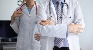 Erkek ve kadın doktor hastane ofiste ayakta close-up. Çapraz kolları ve stetoskop tutan kadın ile ayakta adam. Beyaz tıbbi önlük giyen doktorlar