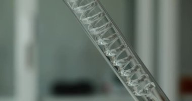 Test tüpünün içindeki sarmal tüpten yavaşça akan temiz sıvının yakın görüntüsü. Laboratuvarda sıvı arıtılıyor