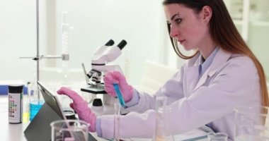 Bilimadamı test sonuçlarını dijital tablete yazar ve laboratuardaki test tüpünde mavi sıvıyla birlikte tutar. Araştırma yapan laboratuvar çalışanı, sağlık ve tıbbi yenilikler için biyokimya analizi yapıyor.