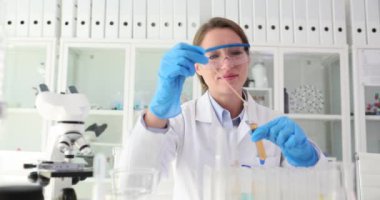 Bilim adamı test tüpünde cam çubukla sarı sıvıyı karıştırıyor. Laboratuvarda zehirli çözücüler test ediliyor.