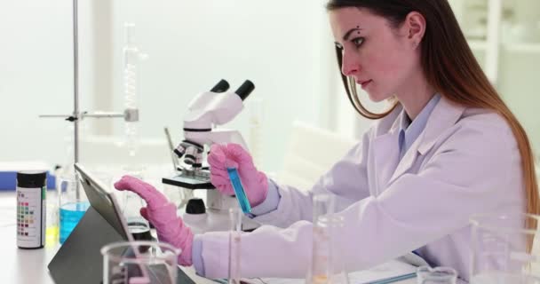 科学家在数字平板上写下测试结果 并在实验室将蓝色液体样品保存在试管中 从事研究的实验室工作人员分析用于保健和医疗创新的生物化学 — 图库视频影像