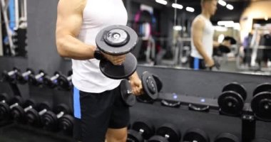Adam spor salonunda kollarını dambıllarla kaldırıyor. Vücut geliştirme için fiziksel ve kas eğitimi