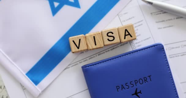 旅行代理店でビザに関する情報を記入するためのフォーム 空白の紙シートと小さなイスラエルの国旗の木製の立方体とパスポートからの単語ビザ — ストック動画