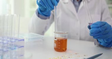 Profesyonel bir laboratuvar çalışanı cam kap iletme deneyinde test reaktifi örneklerini karıştırır. Hafif klinikte sıvıları yavaş çekimde karıştırmak