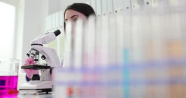 Çalışma alanında oturan kadın bilim adamı örnek incelemek için mikroskoba bakıyor. Tıbbi tesisteki kadın işçiler ağır çekimde deneyler yapmak için donanımlı.