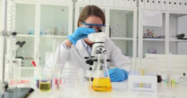 Güvenlik gözlüklü kadın bilim adamı mikroskop aracılığıyla test örneği üzerinde çalışıyor. Laboratuvar uzmanının çalışmalarından iyi sonuç.