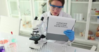 Kadın bilim adamı not defterine mikroskop aracılığıyla kanser aşısı araştırması yazan notlar yazıyor. Kanser tedavisi seçeneği bulunması