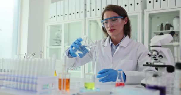 女性化学者は 顕微鏡を用いた軽い実験室での実験のためにガラスフラスコにサンプルを採取する 集中と研究の遅い動きを実行する — ストック動画