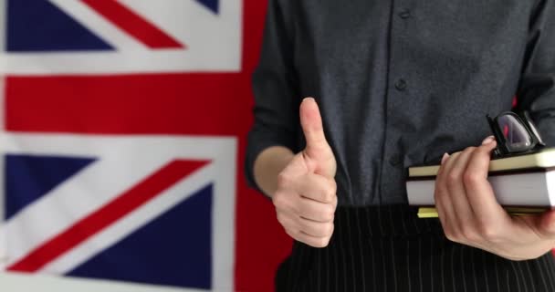 教科書で言語学習を促進する女性 英語の講師は 学校の遅い動きの承認として親指を示す英国の旗の前に立っています — ストック動画