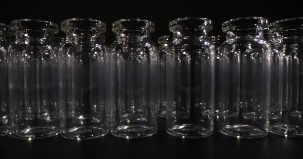 ワクチンのための空のガラス瓶は暗い前提で机の表面の列に立っています 医療目的および実験室調査のための専門のガラス器具 — ストック動画