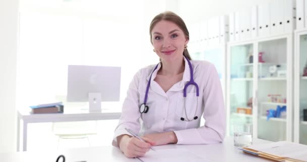 ポジティブな女性医師は 機器付きのクリニックで患者との会談が成功した後 ノートを取ります 職場でのステスコープのスペシャリスト — ストック動画